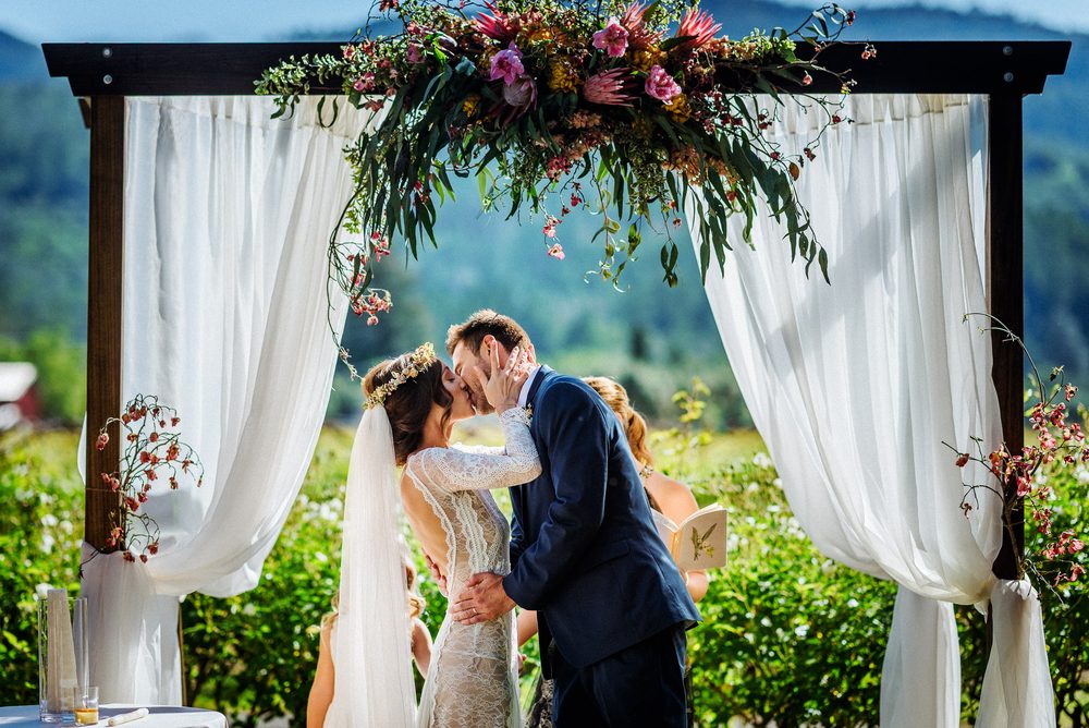 Napa Valley wedding photography of a bride and groom kissing beneath a floral ceremony arch